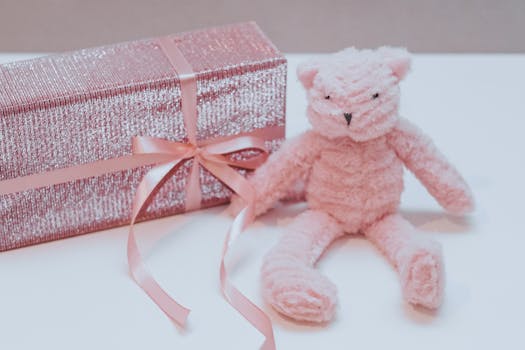 Cadeau mode avec un ours en peluche rose et un paquet scintillant orné d'un ruban rose.